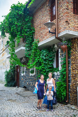 Obraz premium Two young women and a little girl on a background of an ancient building overgrown with ivy. Family portrait outdoors. Women in the old town. Vertical shot.