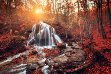 Waterfall. Colorful landscape with beautiful waterfall at mountain river in the forest with red foliage at sunset in autumn. Trees with red leaves. Stones with moss in the water. Blurred water. Nature