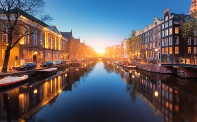 Foto auf Leinwand Colorful cityscape at sunset in Amsterdam, Netherlands. Reflected city lights in water with blue sky at twilight. Night illumination of buildings and boats on the water. Travel. Beautiful street © den-belitsky