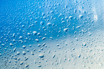 Several water drops on transparent glass and on blue background