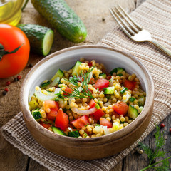 Traditional Israeli healthy meal Ptitim with tomatoes, cucumber and onion for delicious healthy breakfast. Classic Moroccan couscous with vegetables. Top view.