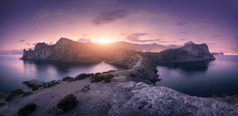 Beautiful mountains against colorful cloudy sky at sunset. Landscape with rocks, sea, mountain trail, forest, purple sky and city lights in summer. Nature and travel. Blurred clouds. Panoramic view
