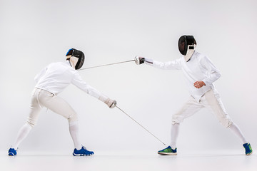 The two men wearing fencing suit practicing with sword against gray