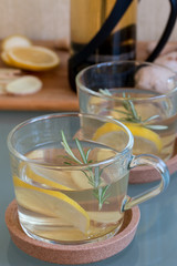 Green tea with lemon,ginger and rosemary in glass cup on the glass table.