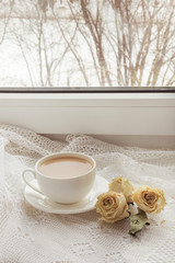 Cup of coffee with milk on windowsill with dry rose  as decor on lace. Vintage.