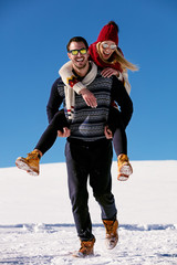 Couple playing in snow. Man giving woman piggyback ride on winter vacation.