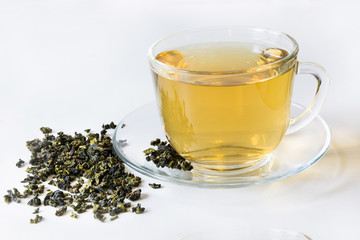 Glass cup with green tea and dry leaves of green tea on white background.