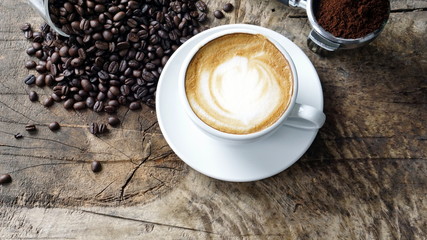 Cappuccino Coffee. A cup of latte, cappuccino or espresso coffee with milk put on a wood table with dark roasting coffee beans. Drawing the foam milk on top.