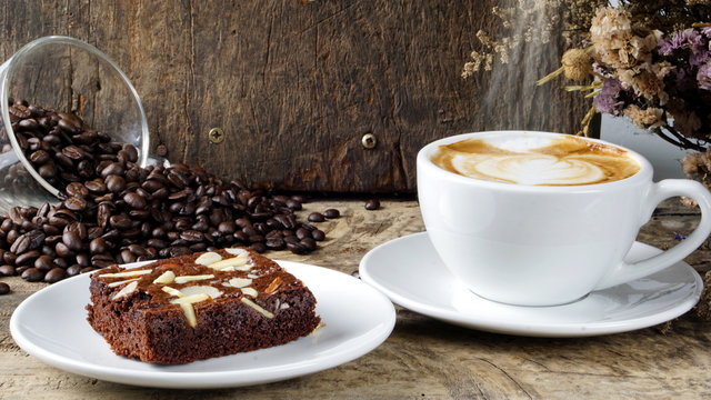 Cappuccino Coffee and sweet chocolate brownies cake. A cup of latte, cappuccino or espresso coffee with milk put on a wood table with dark roasting coffee beans. Drawing the foam milk on top.