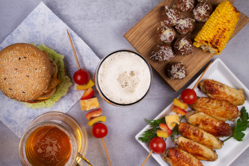Glasses of beer with chicken wings, burger, meat balls, grilled corn and vegetables. Beer bites. Ale and food still life. View from above, top studio shot