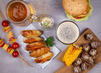 Glasses of beer with chicken wings, burger, meat balls, grilled corn and vegetables. Beer bites. Ale and food still life. View from above, top studio shot