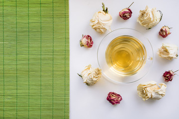 Glass cup of green tea with dry white roses around. Isolated. Toned.
