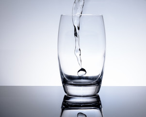 Aufnahme von Eingiessen von Wasser - Mineralwasser in das Glas zum trinken auf weiss - blau...