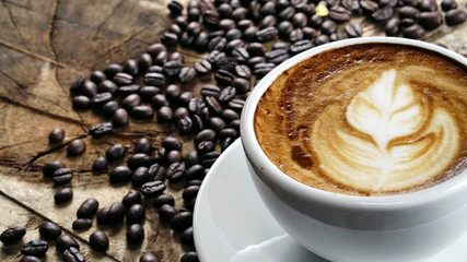 Cappuccino Coffee. A cup of latte, cappuccino or espresso coffee with milk put on a wood table with dark roasting coffee beans. Drawing the foam milk on top.