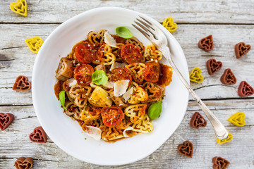 Heart-shaped pasta with tomatoes and basil on wooden background. Italian food on Valentine's Day.
