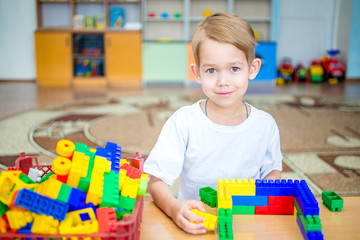 The little boy in the room playing with colorful plastic blocks. Development in the preschool years. Educational games, construction of various facilities. Home, car, engine, garage, transportation.