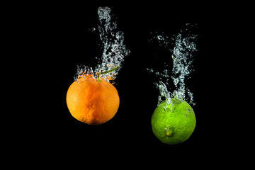 Fototapeta na wymiar Fresh lime and orange in water with air bubbles water splash isolated on black