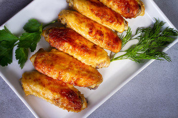 Chicken wings garnished with parsley and dill on a white plate. View from above, top studio shot