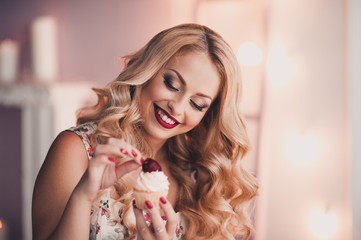 Smiling girl holding cupcake with fresh strawberry on top. Sweet dessert. 20s.