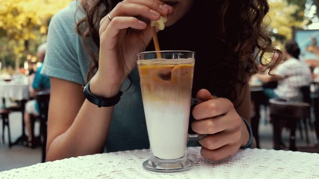 Close-up of a woman in a cafe drinking coffee with milk and ice outdoors