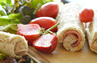 bread stuffed pork bologna roll with cut strawberry and vegetable on wooden chop block