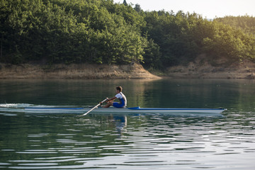 A Young single scull rowing competitor paddles on the tranquil lake