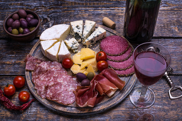 Red wine in a bottle, cork, bottle screw and a set of products - cheese, grapes, nuts, olives, figs on a wooden board, background