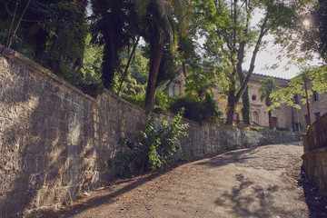 The old mountain road with stone wall to the building through the trees