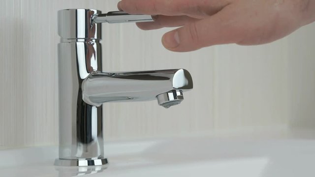 Male hands closing chrome-plated tap of water. Close-up