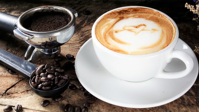 Cappuccino Coffee. A cup of latte, cappuccino or espresso coffee with milk put on a wood table with dark roasting coffee beans. Drawing the foam milk on top.