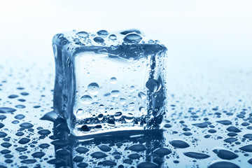 Transparent ice cube with reflection on blue glass with water drops