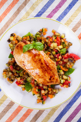 Chicken breast with sauteed vegetables: eggplant, carrot, zucchini, squash and tomatoes. View from above, top studio shot