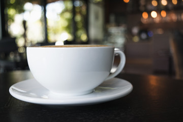 White cup of coffee on wooden table in the coffee shop.