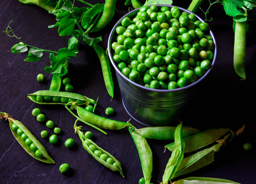 Green pea pods in a tin on black background