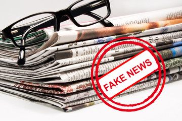 Stapel mit Zeitungen und Stempel Fake News