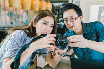 Young Asian couple learning to use mirrorless digital camera together at coffee shop, modern gadget technology concept, focus on the girl, depth of field effect