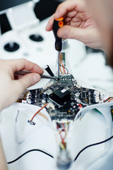 Closeup top view shot of male hands unscrewing circuit board of disassembled drone on white table with assorted tools