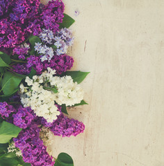 Border of of fresh lilac flowers and green leaves on white wooden background with copy space, retro toned