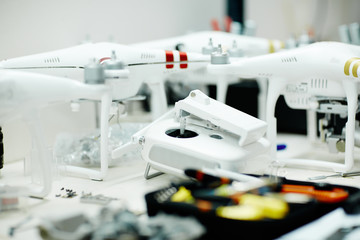 Several high-tech drones standing on white table in modern workshop with controller and assembling tools in front