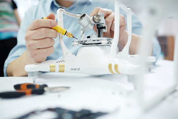 Closeup shot of male hands attaching camera slate to quadrocopter drone on table with different tools in modern workshop