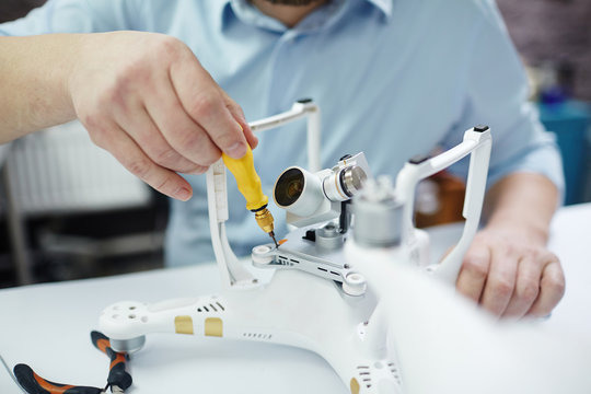 Closeup shot of unrecognizable man working on assembling new spy system using quadrocopter drone on table with different tools in modern workshop