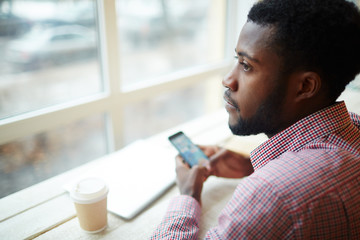 Young entrepreneur with smartphone and drink sitting in cafe