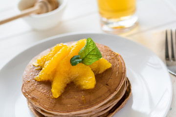 Traditional breakfast: stack of pancakes with orange slices and sweet sauce on white wooden table. Selective focus