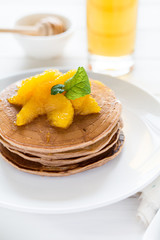 Traditional breakfast: stack of pancakes with orange slices and sweet sauce on white wooden table. Selective focus