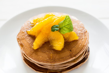 Traditional breakfast: stack of pancakes with orange slices and sweet sauce on white wooden table. Selective focus