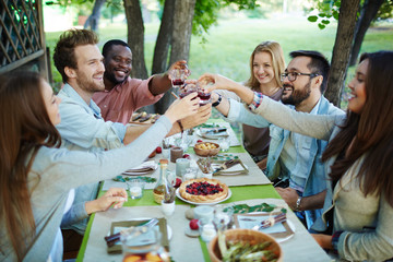 Happy friends with glasses of red wine toasting by festive table