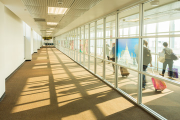 Passengers walking on walkway to airplane. This part of airport building serves a concourse function.