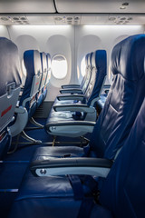 Airplane windows and blue seats in cabin. Economy class on board flight.