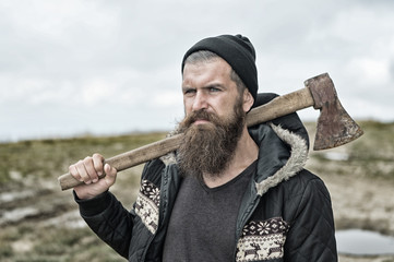 bearded handsome serious man with rusty axe on mountain top