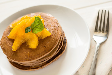 Traditional breakfast: stack of pancakes with orange slices and sweet sauce on white wooden table. Selective focus